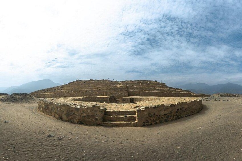 A circular ancient ruin with a central staircase, surrounded by a desert landscape with mountains in the background. 4