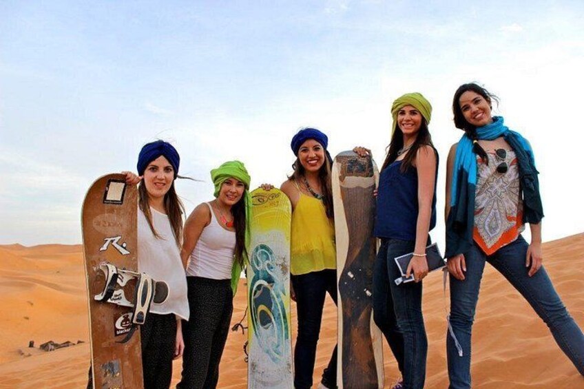 A group of people standing on a sandy beach with snowboards. 1