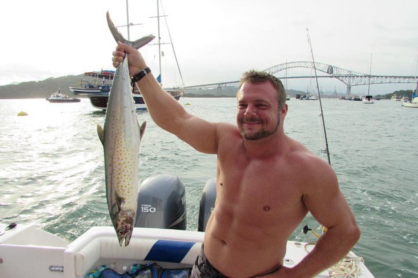 A man holding a fish on a boat with a bridge in the background. 1