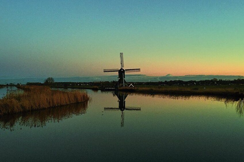 Eine Windmühle am Ufer eines ruhigen Gewässers unter einem wolkenlosen Himmel. 2
