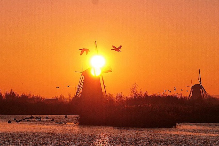 Ein Sonnenuntergang über einem Gewässer, mit im Himmel abgebildeten Windmühlen. 1