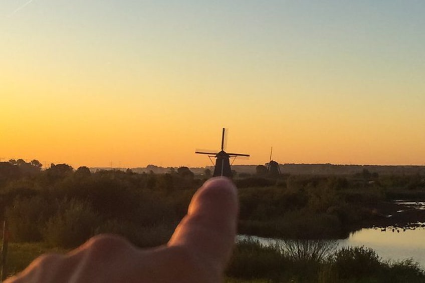 A hand pointing towards windmills in a sunset landscape. 2