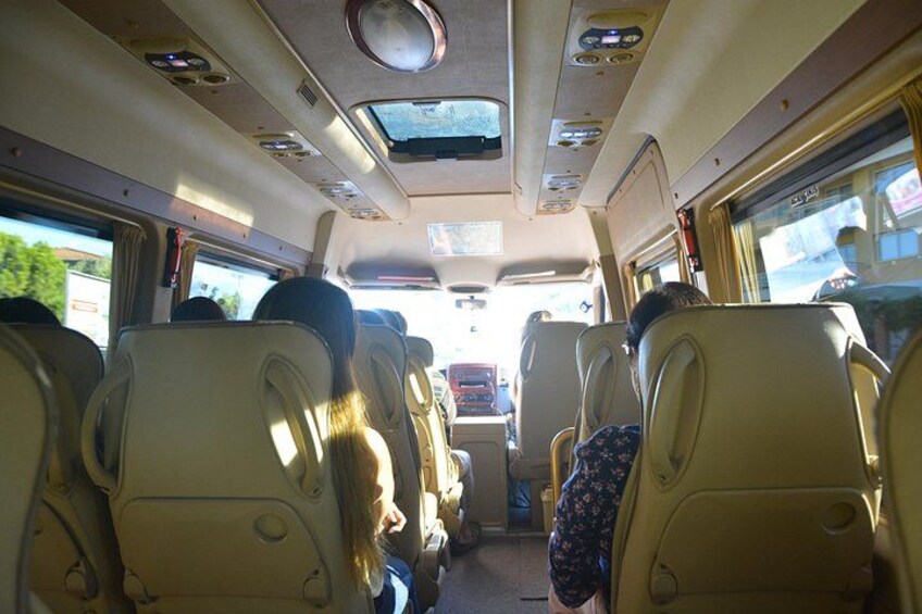 The interior of a bus with beige seats, overhead compartments, and a sunroof. 2
