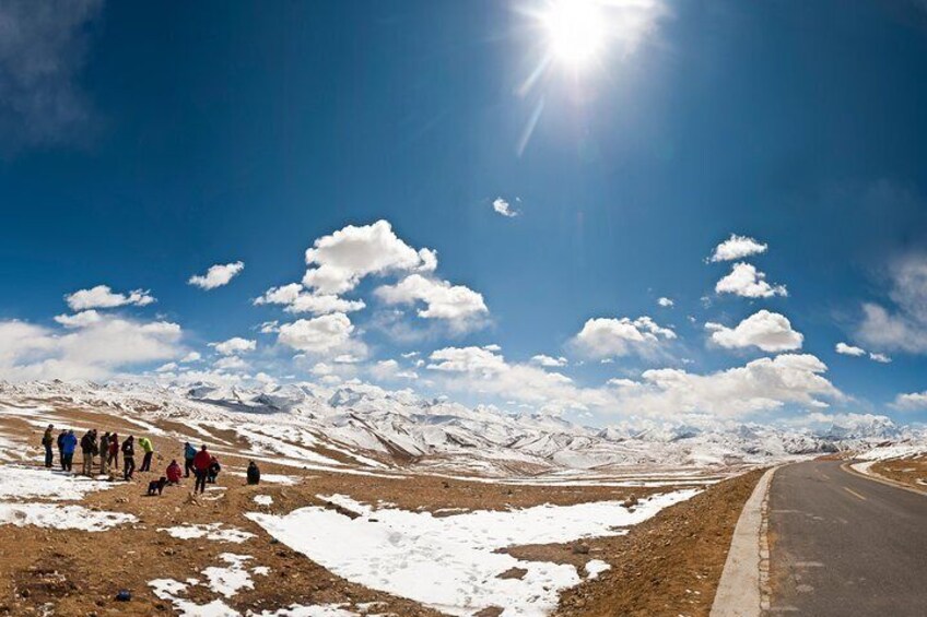 A group of people on a mountain road with snow patches and a clear sky. 3