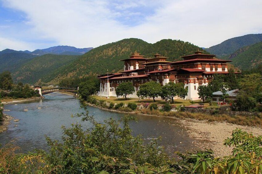 A traditional multi-tiered building by a river, surrounded by lush greenery and mountains. 4