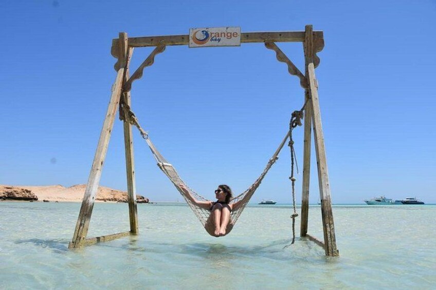 Una estructura de columpio de madera en agua cristalina con una persona colgando. 2