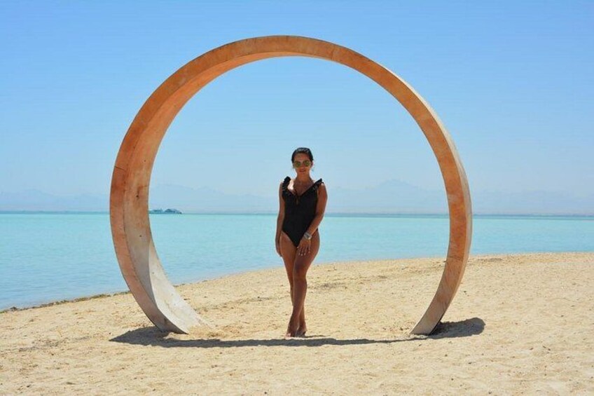 Una persona parada en una zona de playa arenosa con una gran estructura metálica circular al fondo. 3
