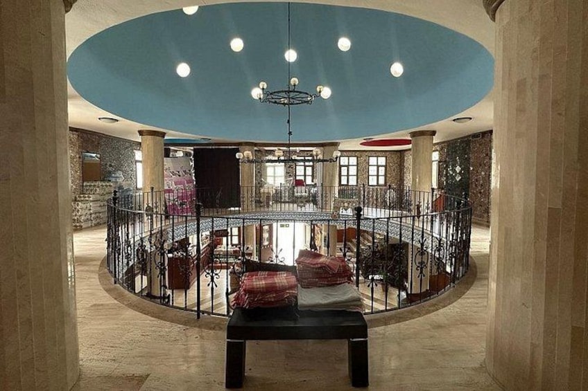 A spacious lobby with a central seating area, a high ceiling with a blue accent, and a grand staircase. 3