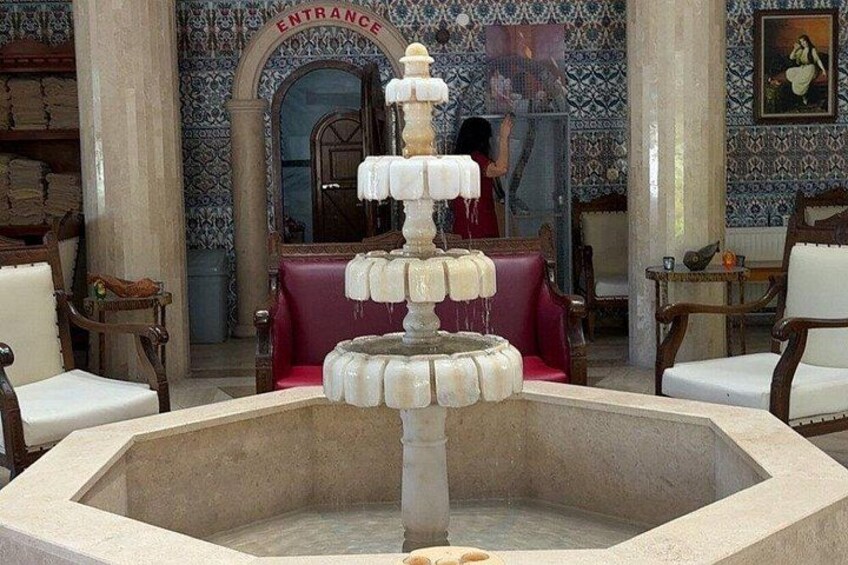 A fountain with multiple tiers in a room with patterned walls and red seating. 5