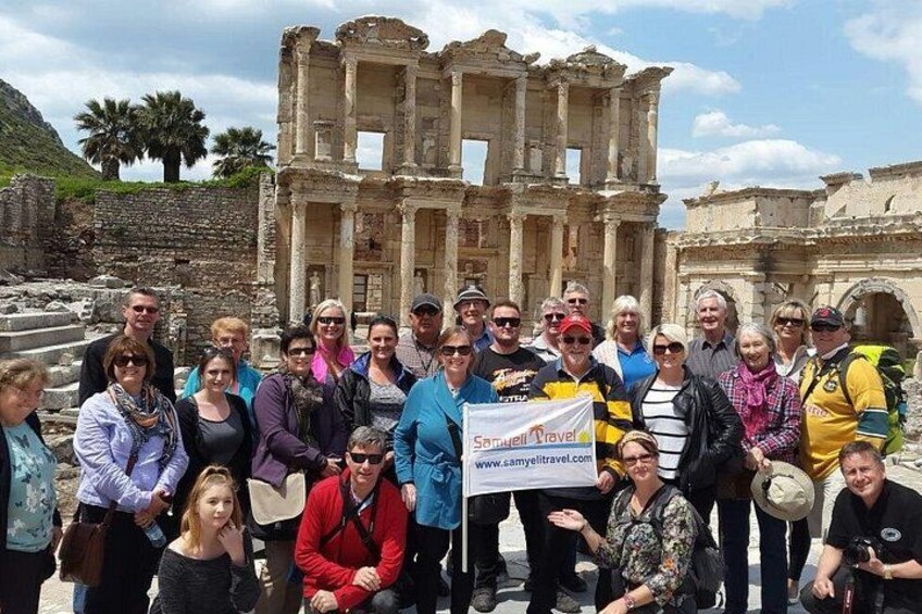 A group of people standing in front of ancient ruins with columns and arches, some holding a banner. 1