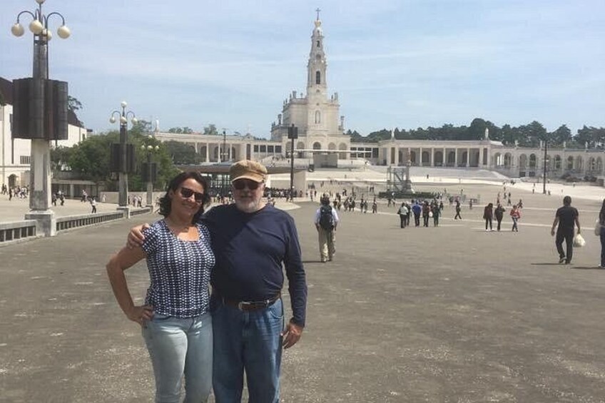 A couple standing in a plaza with a large building and a tower in the background. 2