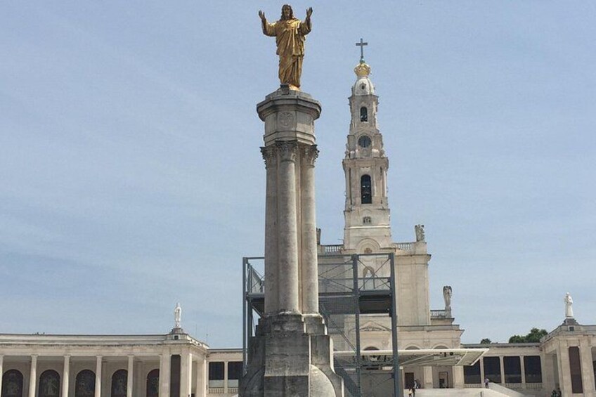 A large golden statue atop a column in front of a church with a bell tower. 4