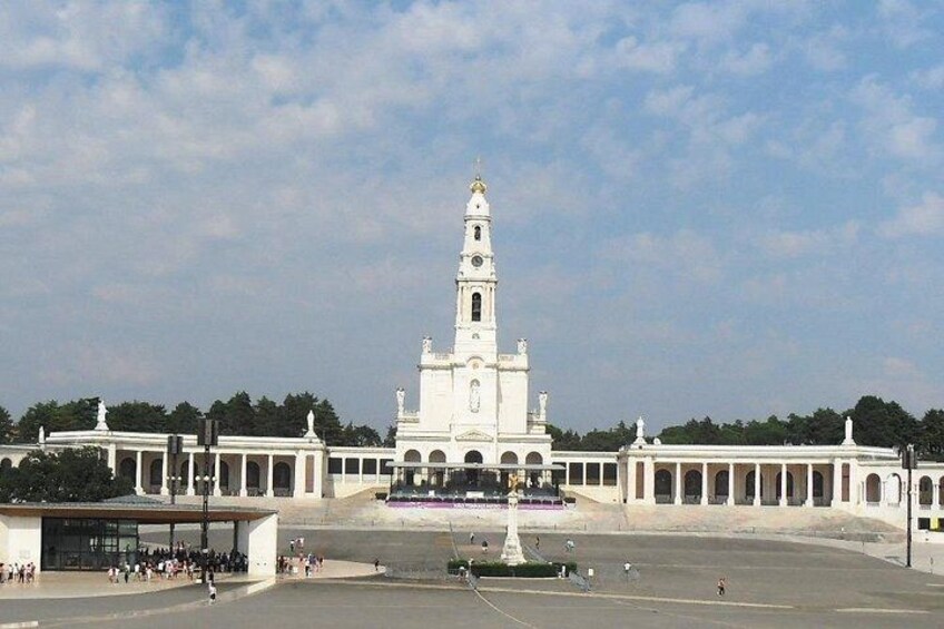 A large white building with a tall tower, surrounded by a paved area and a row of smaller structures. 3