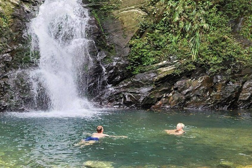 A waterfall, clear water, and two people swimming. 4