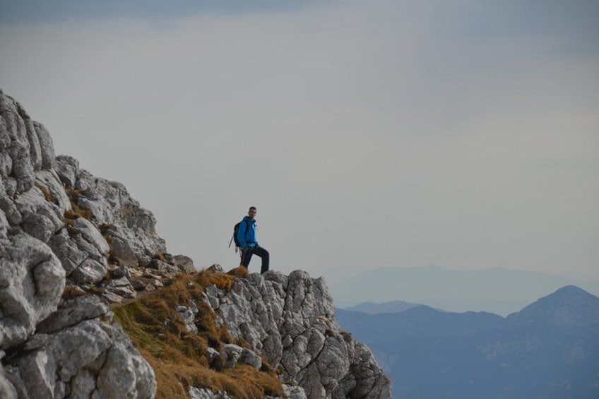A person standing on a rocky outcrop with a mountainous landscape in the background. 1