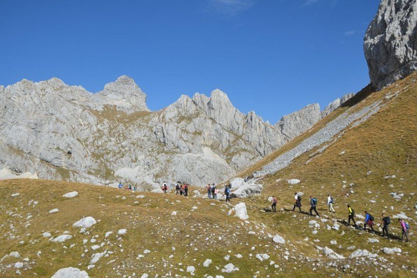 A group of hikers on a mountain trail with rocky terrain and sparse vegetation. 3