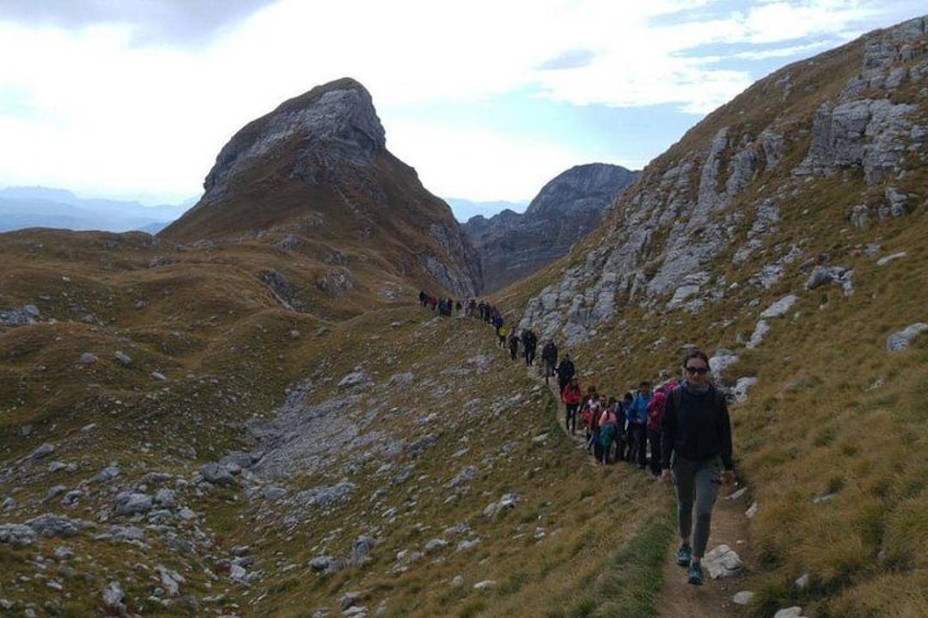 A group of hikers on a mountain trail with rocky terrain and a prominent peak in the background. 4