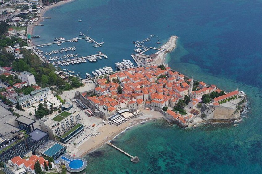 An aerial view of a coastal town with a prominent red-roofed central area, a marina with boats, and a clear blue sea. 4