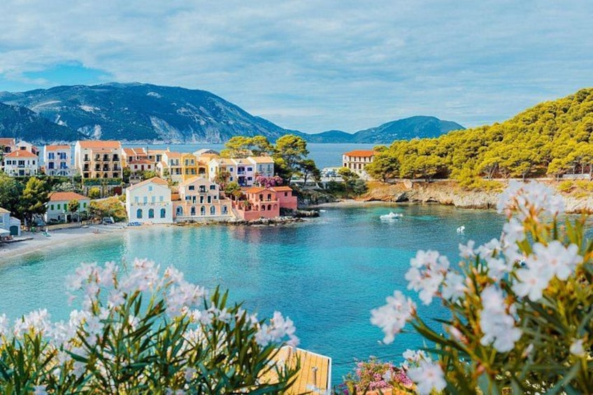 A coastal town with colorful buildings, a clear blue sea, and mountains in the background. 1