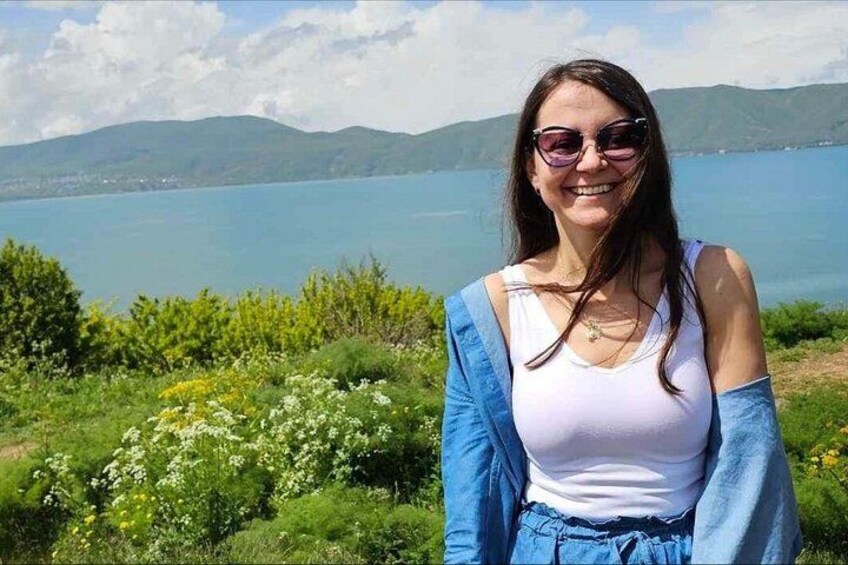 A person standing in a natural setting with a lake and mountains in the background. 2