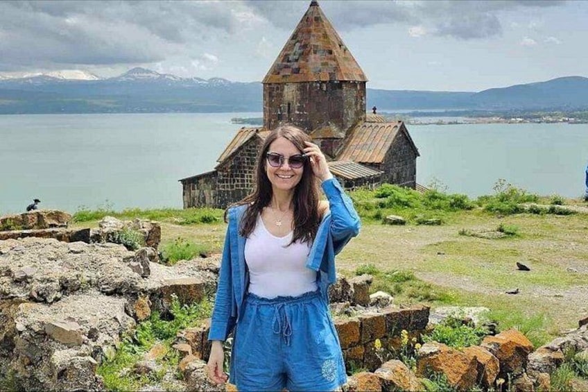 A person standing in front of a historic building with a lake and mountains in the background. 4