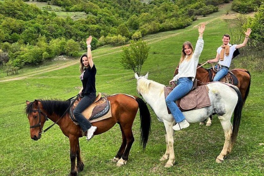 Tres personas montando a caballo en un campo cubierto de hierba, con árboles al fondo. 1