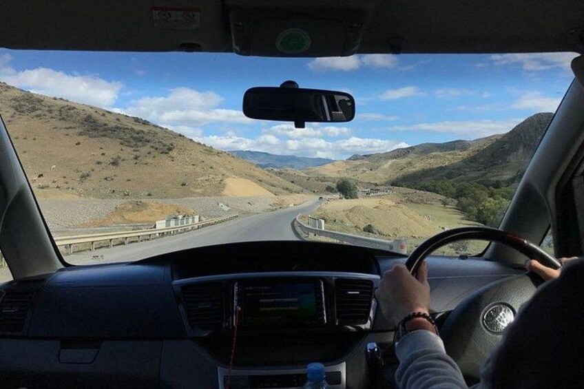 A vehicle driving on a road with a hilly landscape in the background. 1