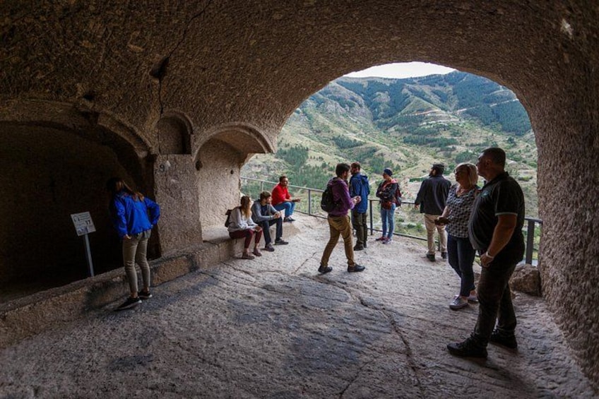A group of people standing in an arched stone structure with a view of a mountainous landscape. 3