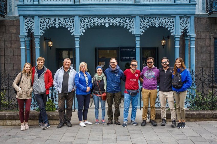 A group of people standing in front of a blue building with ornate architectural details. 2