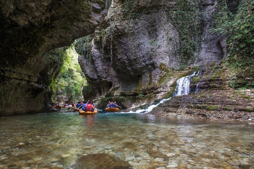 A group of people rafting through a narrow canyon with a waterfall. 2