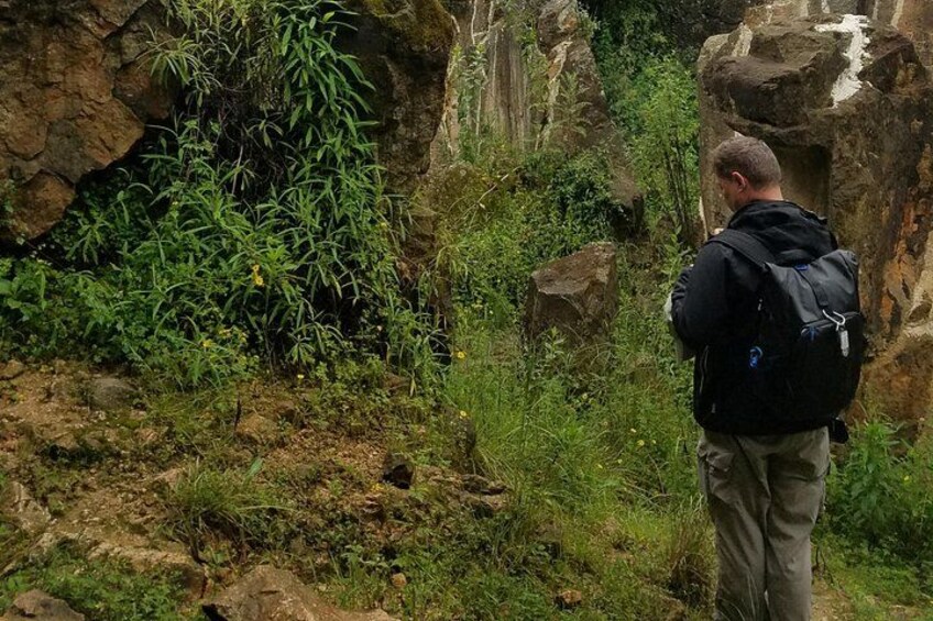 A person standing on a rocky terrain with greenery, wearing a backpack. 5