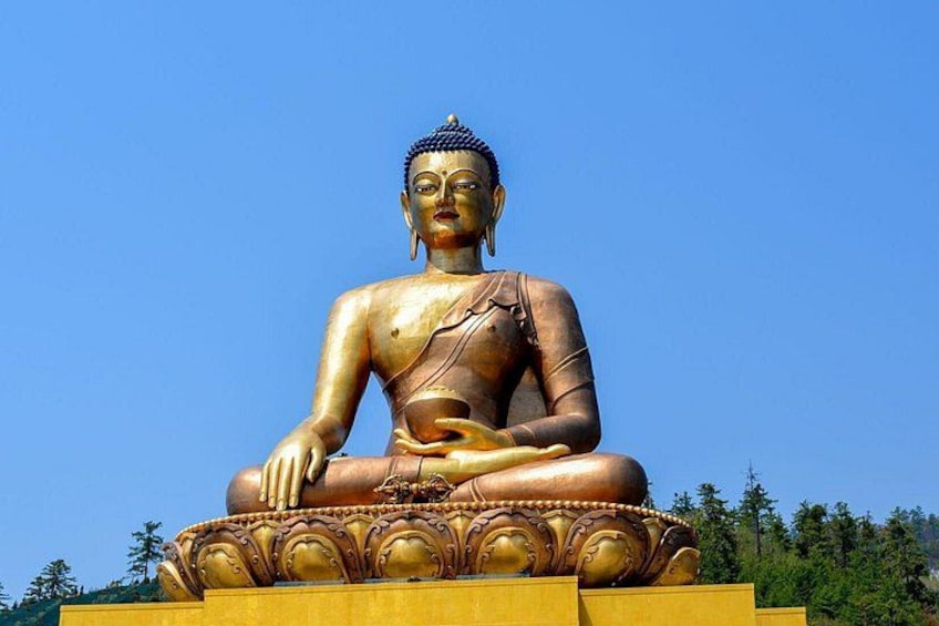 Una gran estatua dorada de Buda sentado sobre un pedestal con diseños intrincados, rodeado de un cielo azul claro y follaje verde. 1