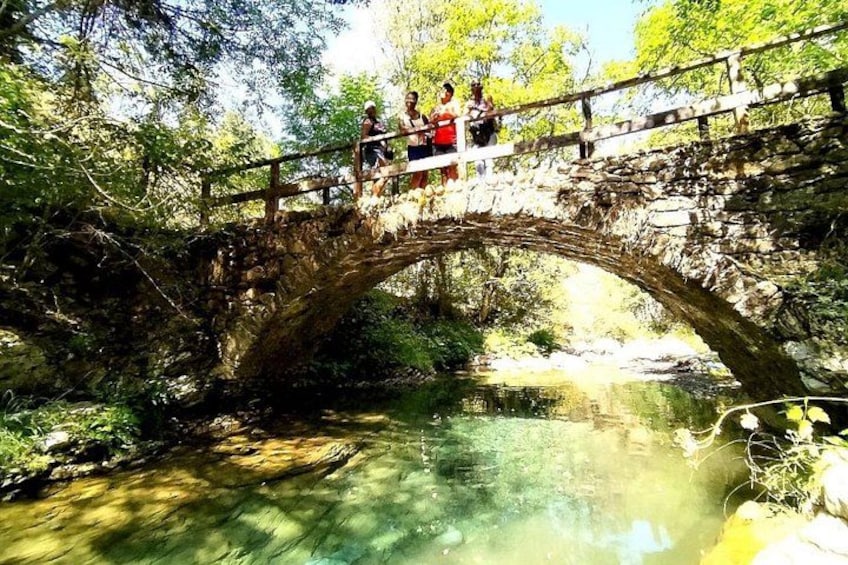 Un pont de pierre enjambe un ruisseau aux eaux claires, le tout étant entouré d’arbres. 4