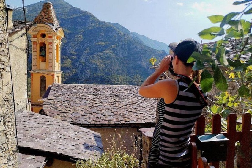 A person taking a photo of a village with a church and mountains in the background. 4