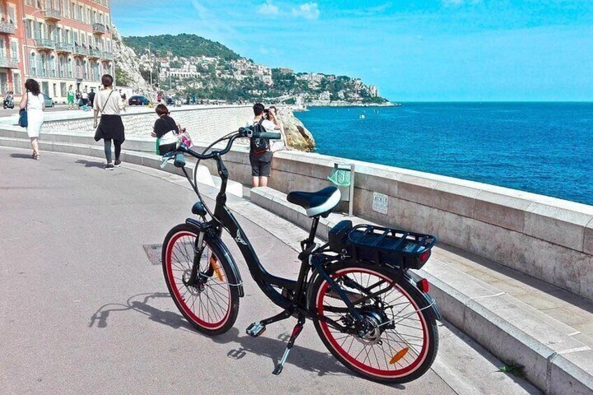 Una bicicleta negra con detalles rojos estacionada en un área pavimentada cerca de la costa. 2
