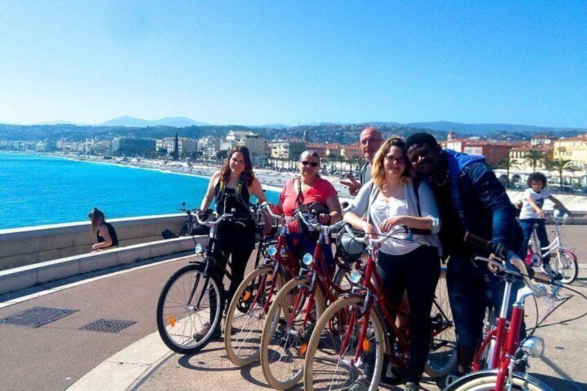 En grupp människor med cyklar står vid en strandpromenad och blickar ut över stadsbilden. 1