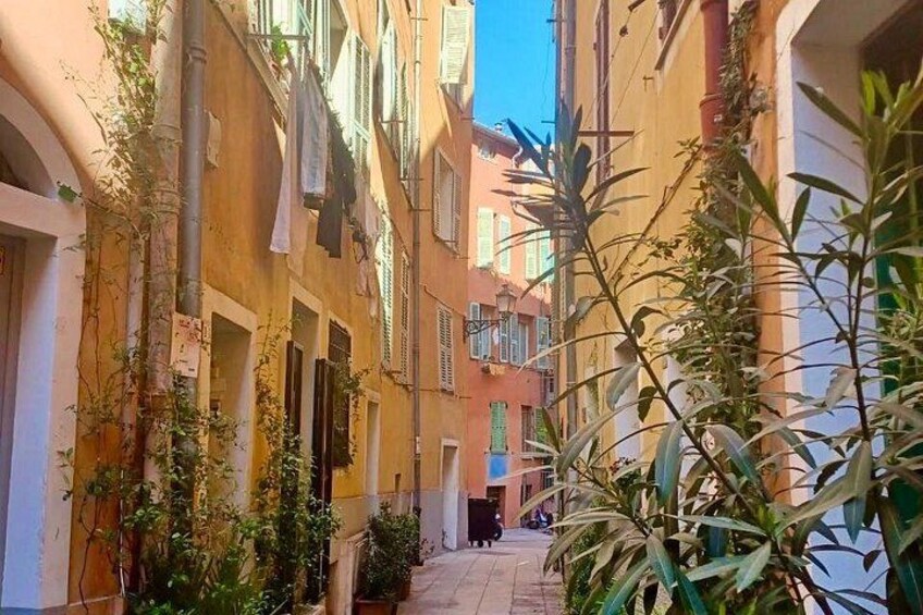 Une ruelle étroite bordée d’immeubles, avec quelques plantes et un ciel dégagé. 2