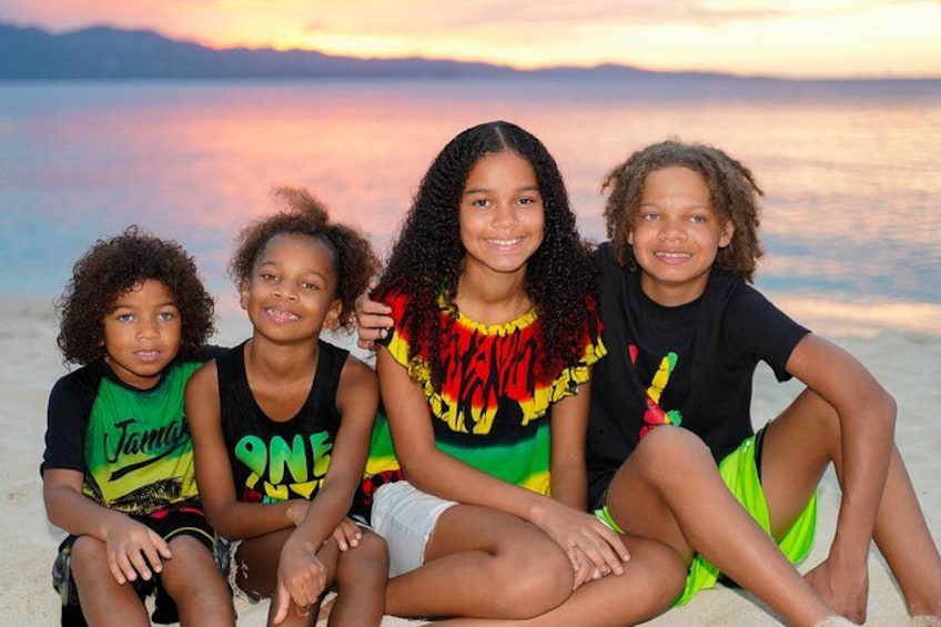 Four children sitting on a beach with a sunset in the background. 5