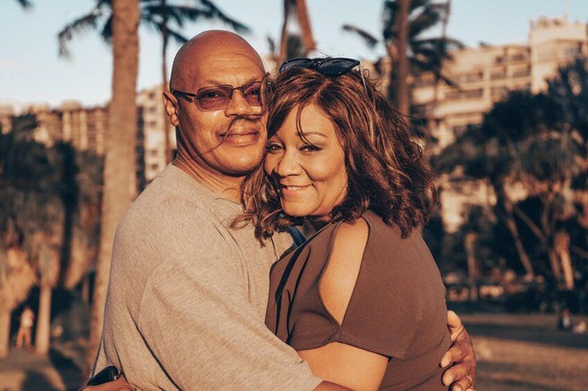 A couple embracing in a park with palm trees and buildings in the background. 3