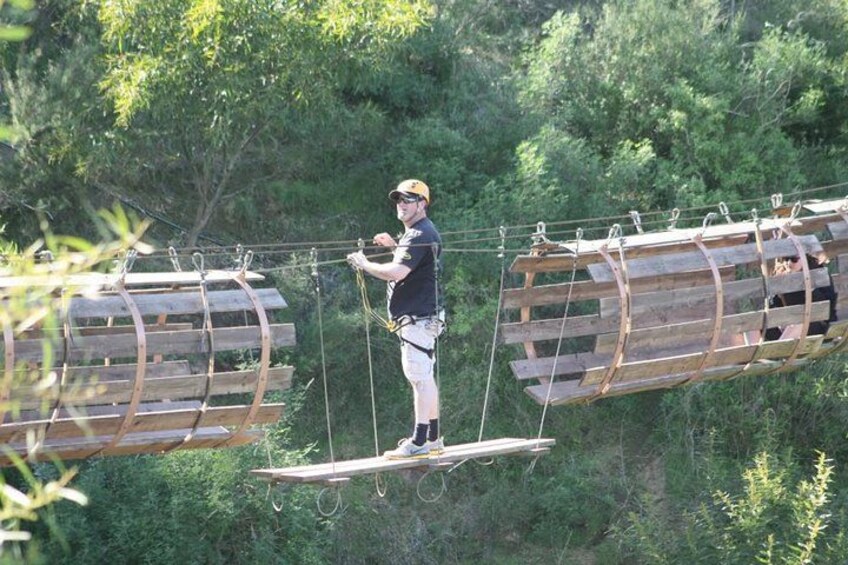 A person on a suspended wooden bridge in a forested area. 3