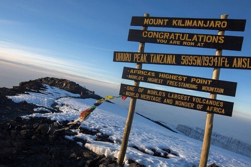 A signpost at Mount Kilimanjaro's Uhuru Peak with congratulatory messages and elevation details. 2