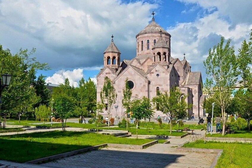A historic church with a prominent dome and bell towers, surrounded by a well-maintained park with trees and a paved walkway. 5