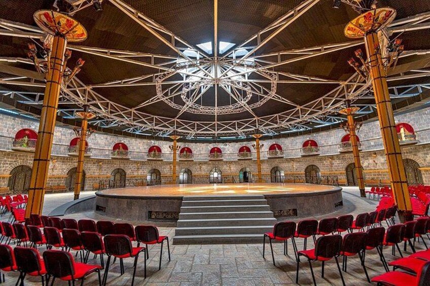 A large hall with a central stage, red chairs, and a high ceiling with a geometric design. 4