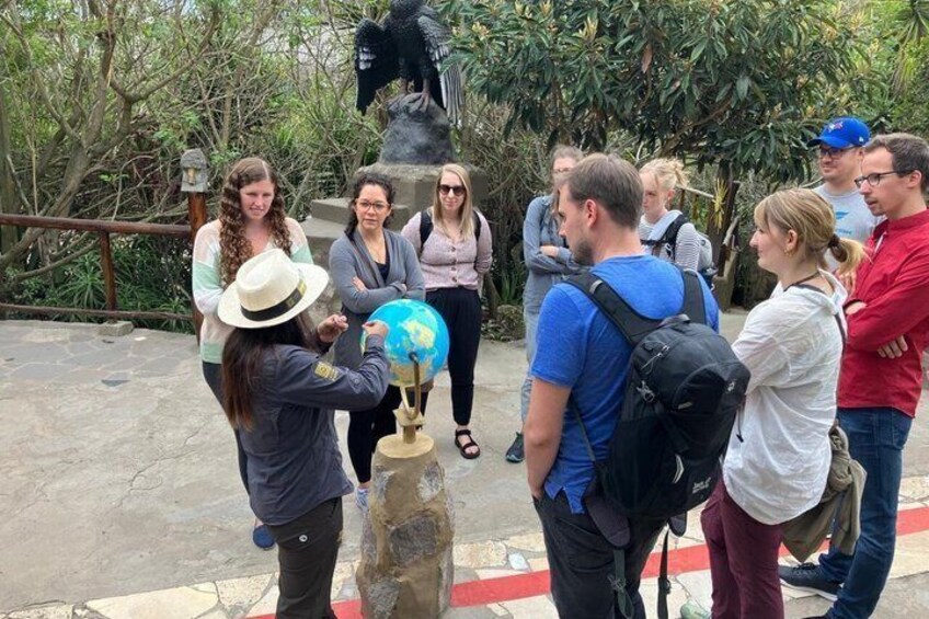 A group of people standing around a globe on a pedestal, with greenery and a statue in the background. 2