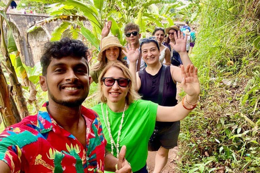 Un grupo de personas caminando por un área boscosa exuberante y verde, con vegetación densa y un muro de piedra al fondo. 5