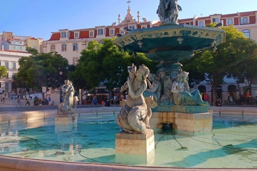 A fountain with statues in a public square with buildings in the background. 4