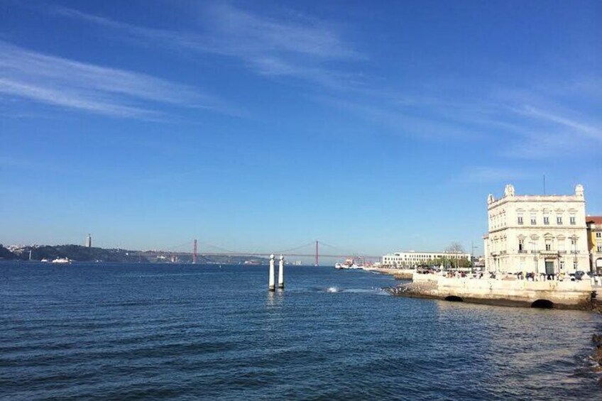 A coastal city with a prominent white building, a red bridge in the distance, and calm waters. 2