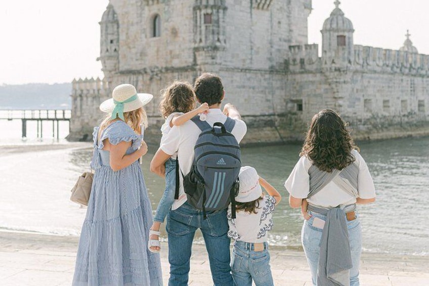 A family of five standing by a waterfront with a historic building in the background. 5