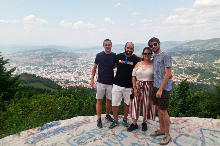 Cuatro personas de pie en una colina, con un paisaje urbano al fondo. 5