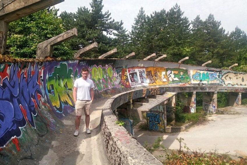 Una persona de pie sobre un sendero de hormigón al lado de un muro con grafitis y un puente con estructuras de madera. 2